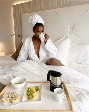 Black woman sitting in bed drinking coffee